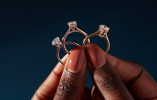A woman holding up three gold engagement rings from Blue Nile