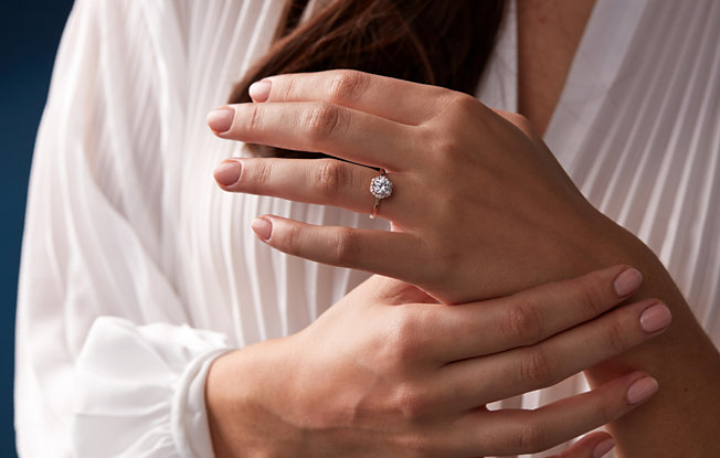 A pair of woman's hands wearing a round cut rose gold engagement ring
