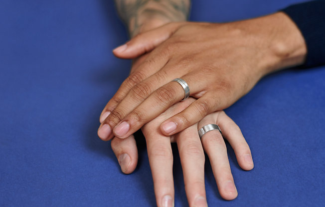Two hands with wedding rings sit on top of one another on a blue background