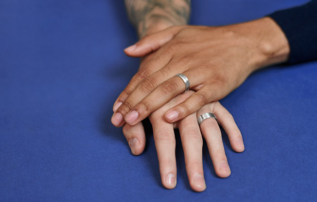 Two men holding hands and wearing silver wedding weddings rings on a blue background