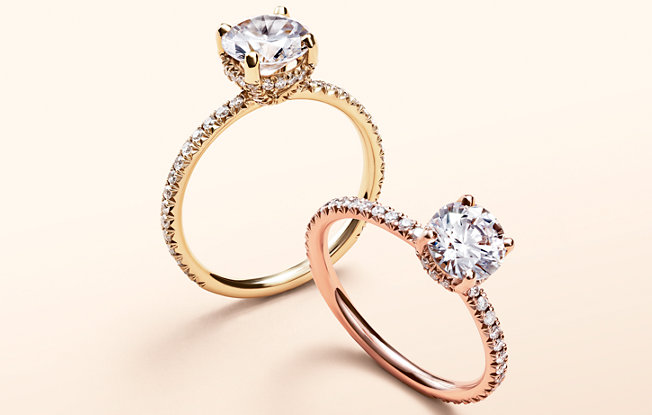 A yellow gold and a rose gold engagement ring with round cut center stones on a yellow background
