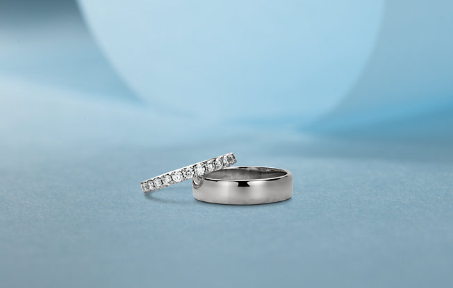 Men's silver wedding ring and woman's diamond engagement ring on a blue background