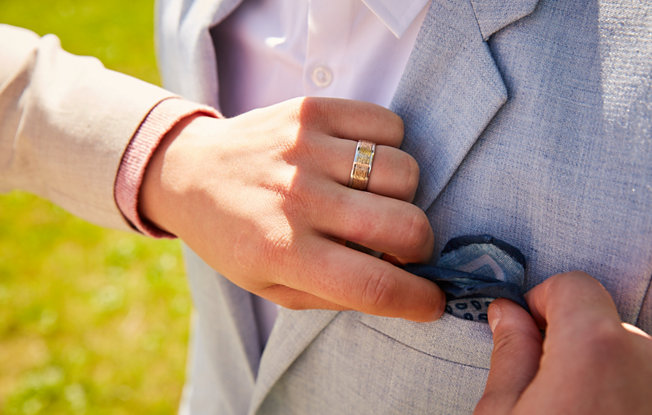 A man wearing a yellow gold textured wedding ring from Blue Nile fixes the pocket square on another man's suit