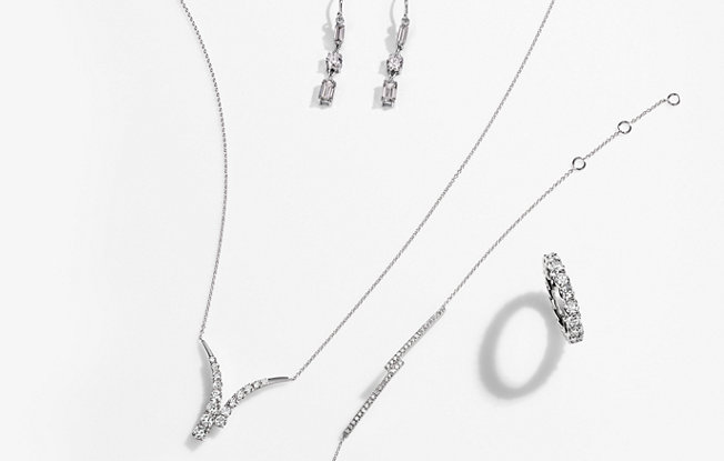 A matching white gold and diamond necklace, earrings, bracelet and ring set on a white background
