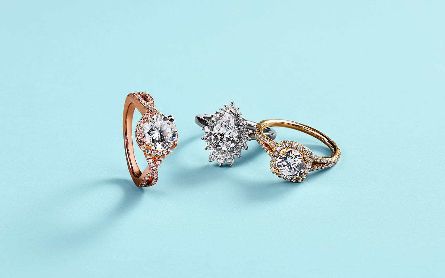 Three diamond and gold engagement rings in white gold, yellow gold and rose gold.
