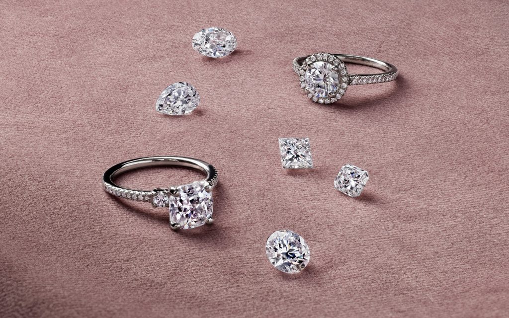 Two diamond engagement rings with loose diamonds nearby, image features both natural and lab made diamonds. 