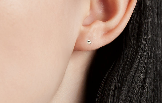 A close up of a woman's ear featuring a yellow gold stud earring