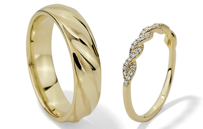 One gold men's wedding ring and one gold women's wedding ring with diamonds on a white background