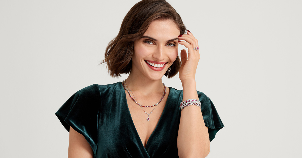 Photo of a smiling woman, she is wearing aesthetic jewelry with Barbiecore motifs in pink sapphires.