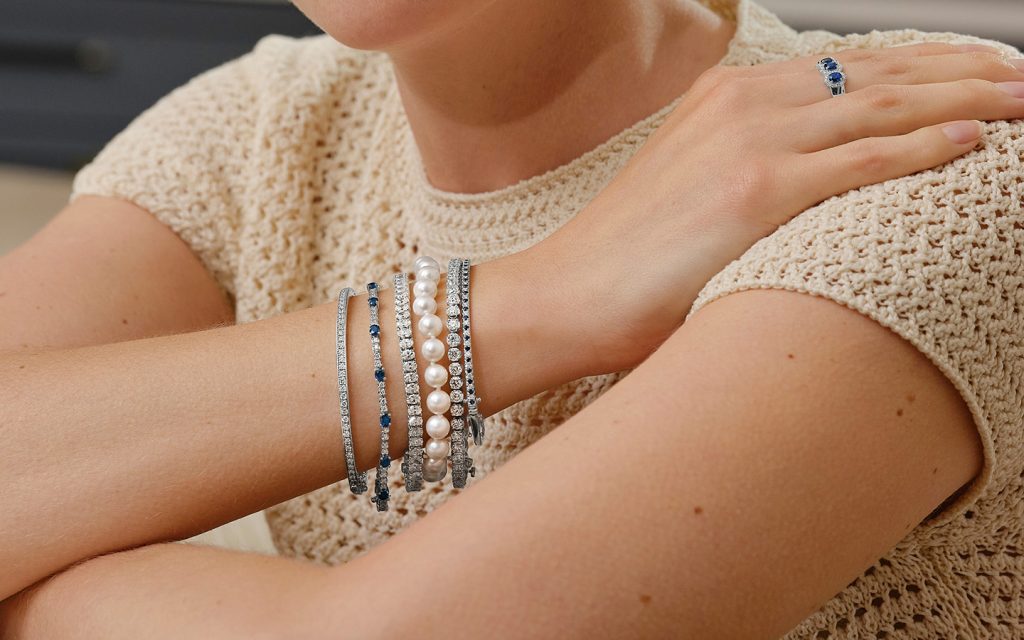 Woman wearing a bracelet stack with gemstone, diamond and pearl bracelets.