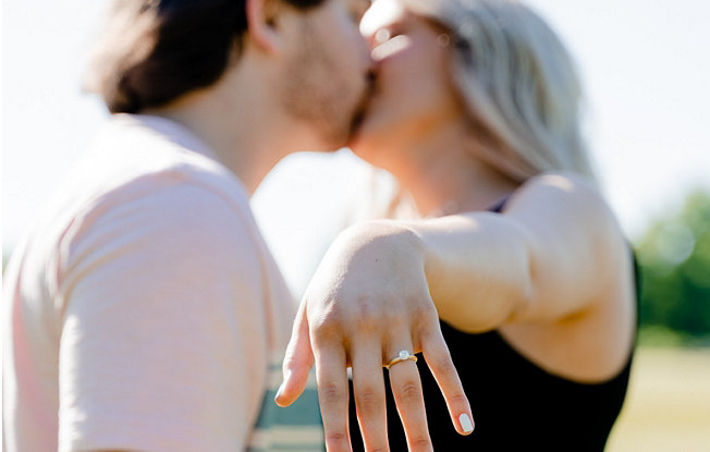 Couple kissing with the woman's engagement ring in the foreground.