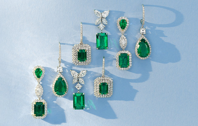 Collection of emerald earrings casting shadows on a blue background