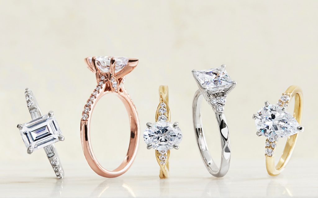 Five platinum, rose gold and white gold diamond engagement rings on a light background. 