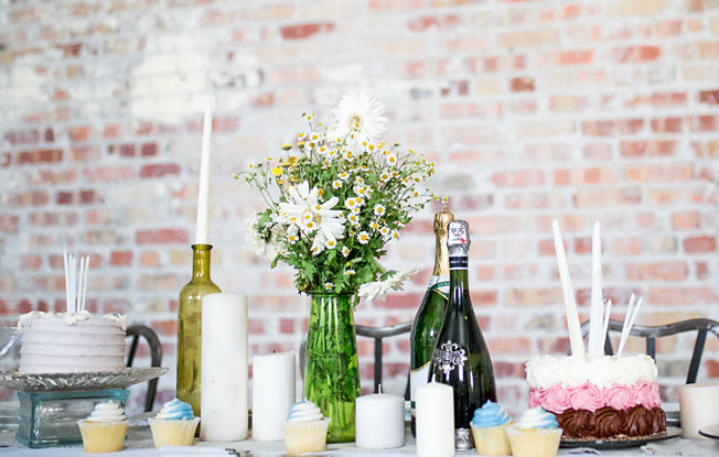 A dessert table set with wine, cupcakes and candles against a brick background