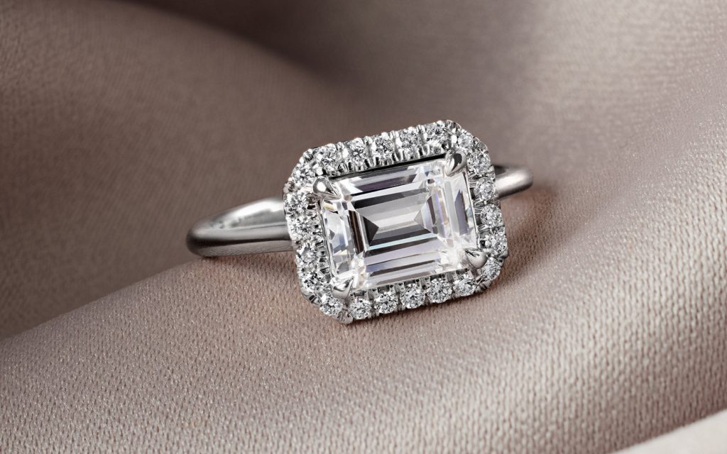 Platinum engagement ring with an east west emerald diamond and halo of diamonds.