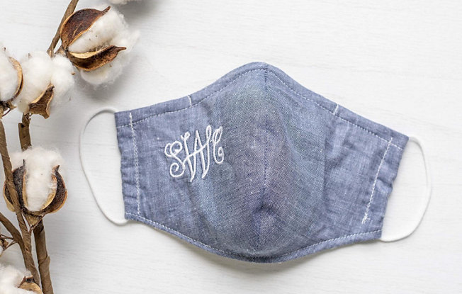 A denim facemask with script initials SWC embroidered in white thread