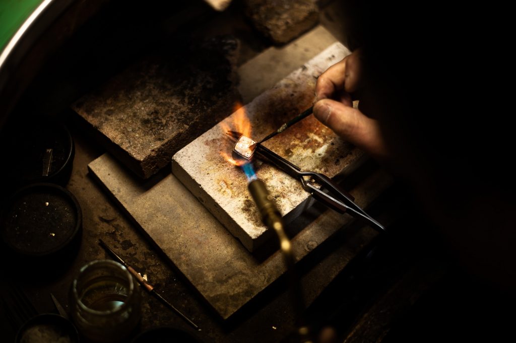 Close up of a piece of jewelry as a bench jeweler works on it with a torch. 