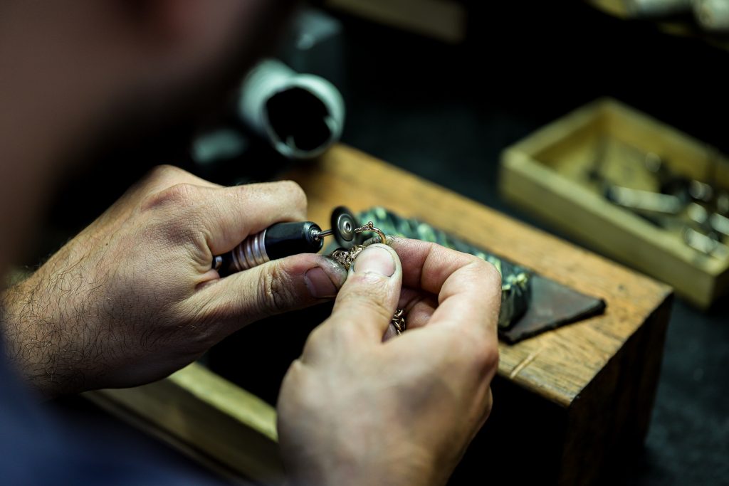 Photo of a jeweler’s hands as they finish a piece of jewelry. 