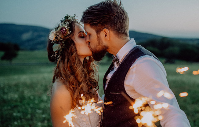 A bride and groom kiss at sunset holding sparklers