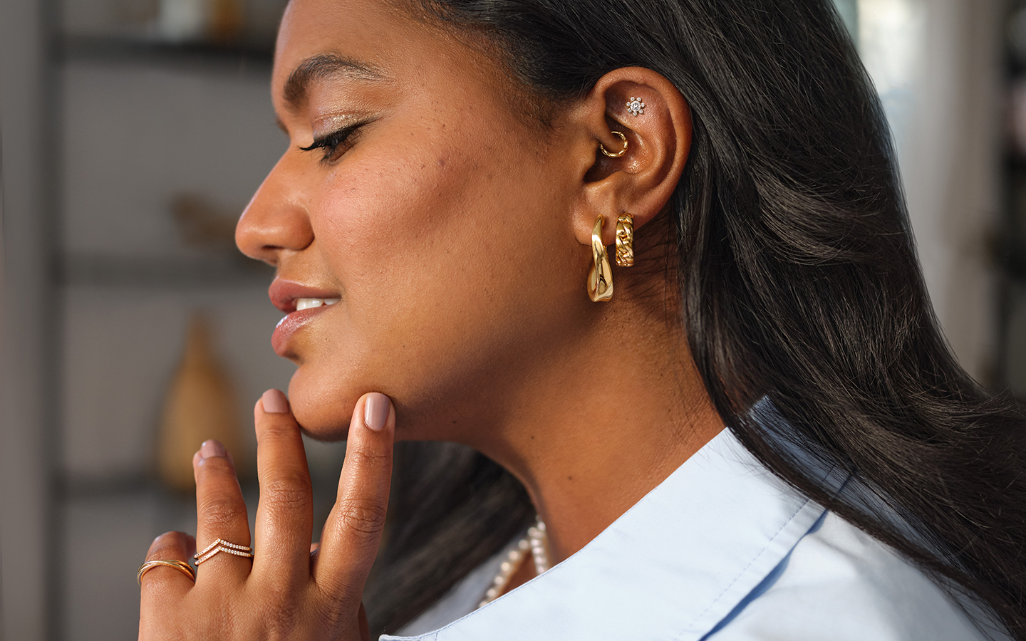 Profile of a smiling woman, she is wearing a maximalist jewelry style with multiple earrings, rings and necklaces.
