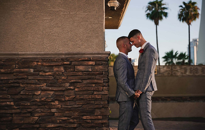 An LGBTQIA+ couple wearing matching suits embracing before their wedding