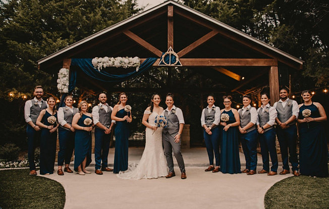 An LGBTQIA+ wedding party stands in front of a barn decorated with flowers