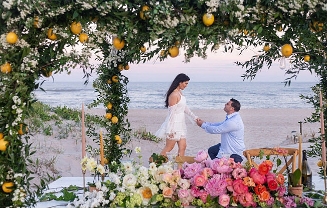 Man proposing to a Woman on a beach surrounded by flowers