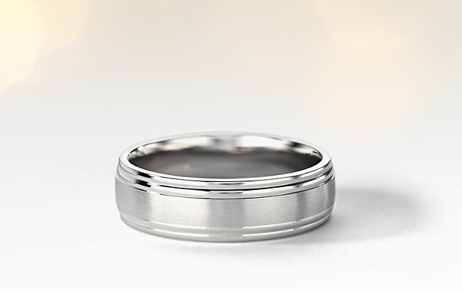 A platinum Blue Nile men's wedding ring sitting on a grey background