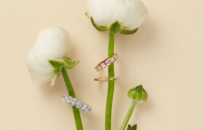 White gold and rose gold eternity bands displayed on the stems of flowers. 