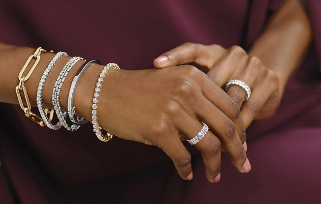 Close up photo of a woman’s hands and forearms. She is wearing bracelets and eternity rings in yellow and white gold with diamonds.