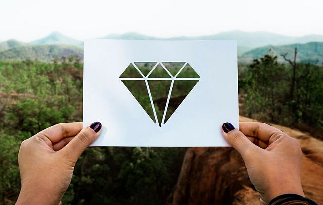 Woman's hands hold a paper cutout of a diamond across a view of the mountains
