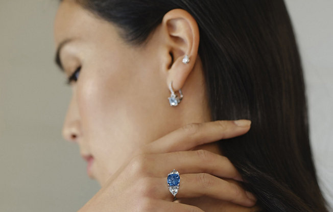 Profile of a woman with her hand on her shoulder, she is wearing a sapphire ring. 