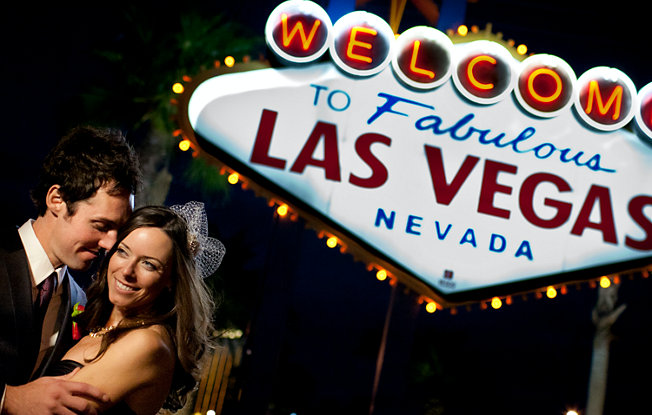 Husband and wife smiling in front of the iconic Welcome to Las Vegas sign.