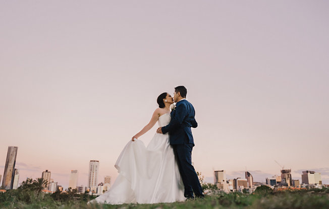 A bride and groom embrace against a city landscape