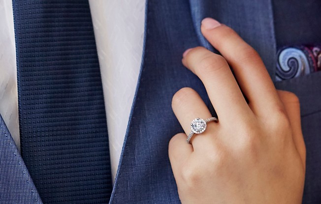 Photo of a woman's hand adjusting a man's blazer, she is wearing an engagement ring 