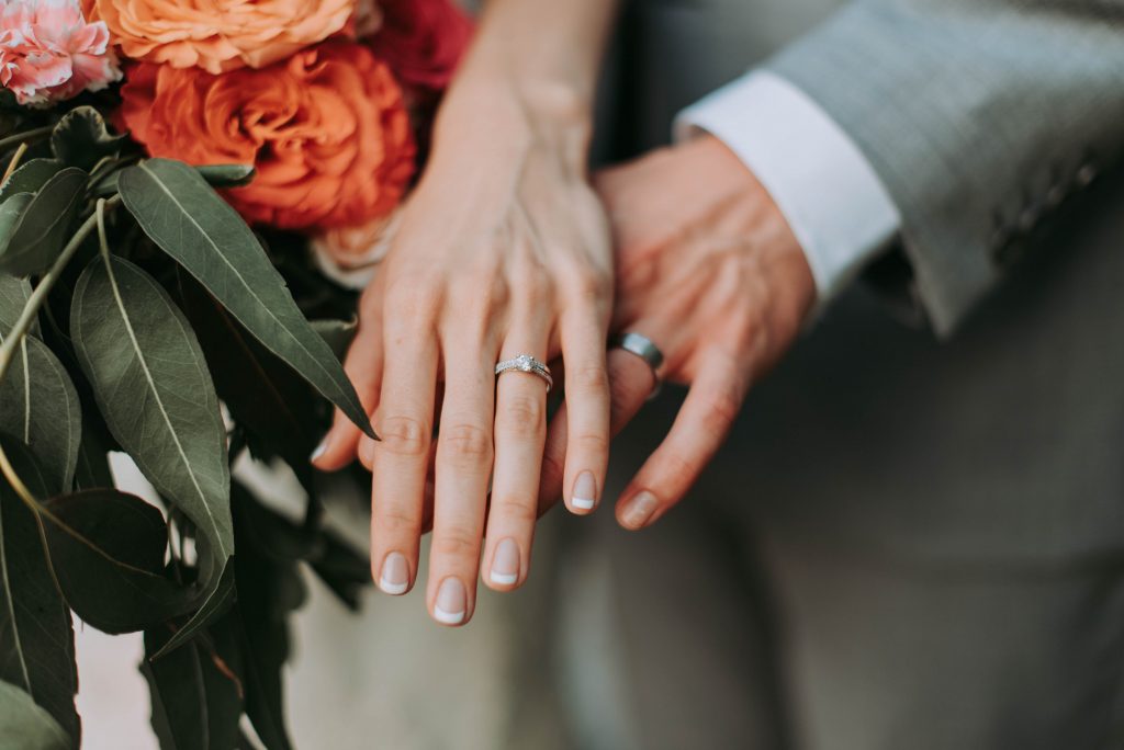 Photo of a bride and groom’s hands together, the bride has a French manicure.