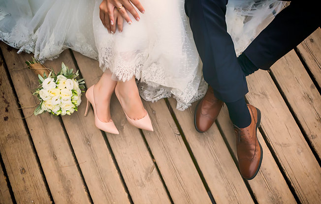 Legs and hands of newlyweds sitting on a wooden deck near bouquet