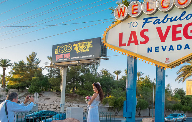 A woman in a wedding dress having her picture taken under the welcome to Las Vegas sign