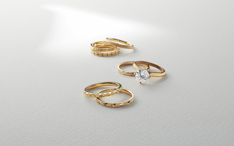 Loose yellow gold bands and diamond engagement ring on a light background.