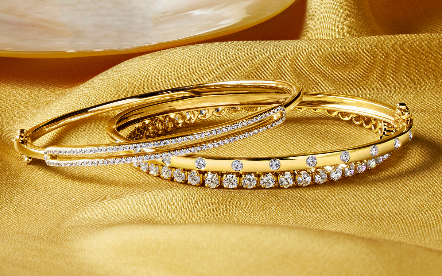 Yellow gold bangle and tennis bracelets on a yellow background. 