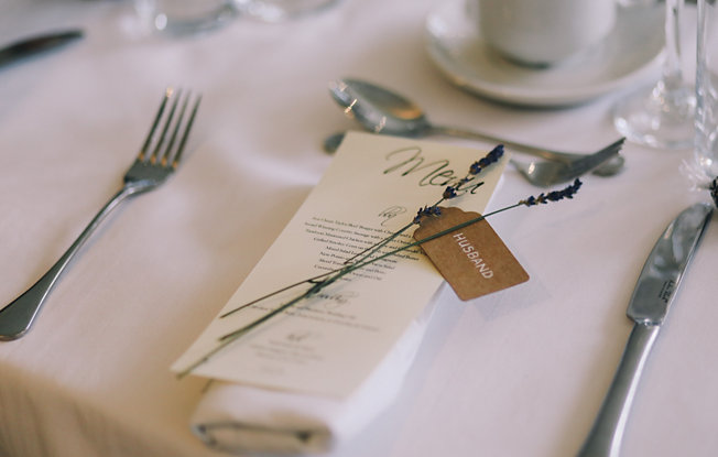A table set with a menu, silverware and lavender on a white table cloth