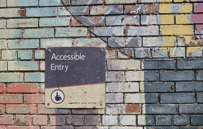 A wheelchair accessible entry sign on a brightly painted brick wall