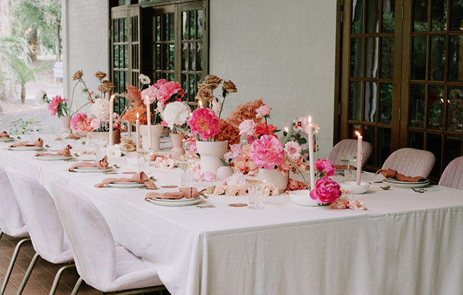 A table dressed with a white tablecloth and bright pink floral arrangements