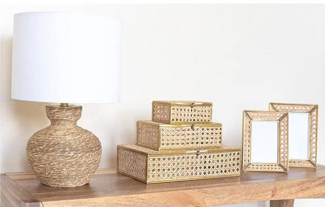 3 woven jewelry boxes, a lamp and matching picturing frame sit on a wooden table from Chairish