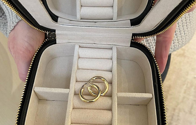 A zip up travel jewelry case with a pair of gold hoop earrings inside