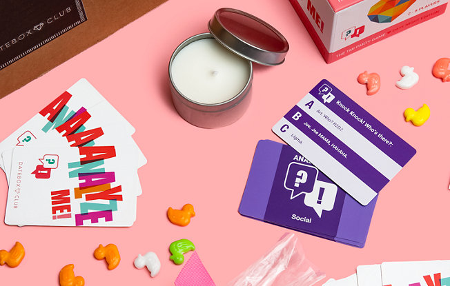 The contents of a Datebox spread out across a table including a candle, card games and candy