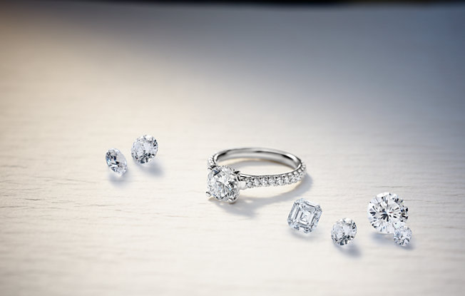 6 loose diamonds and a platinum diamond ring with round center stone and pave setting sit on wooden table