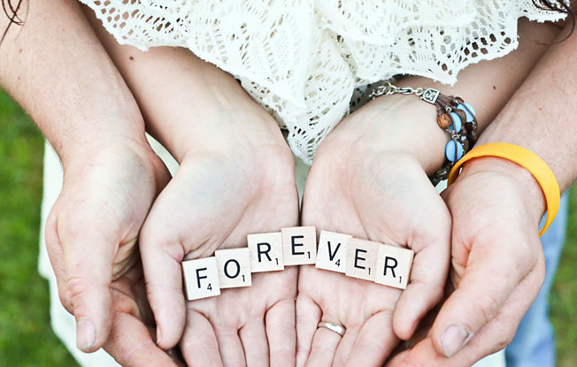 A man and a woman hold scrabble pieces in their hands spelling out the word forever