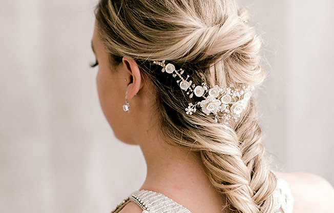 A bride getting ready for her wedding with a french braid updo and floral lace accent in her hair