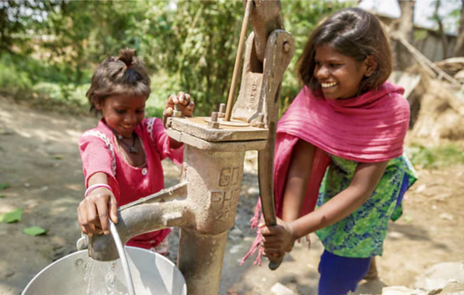 Two young women in India drawing clean water from a well using a manual pump